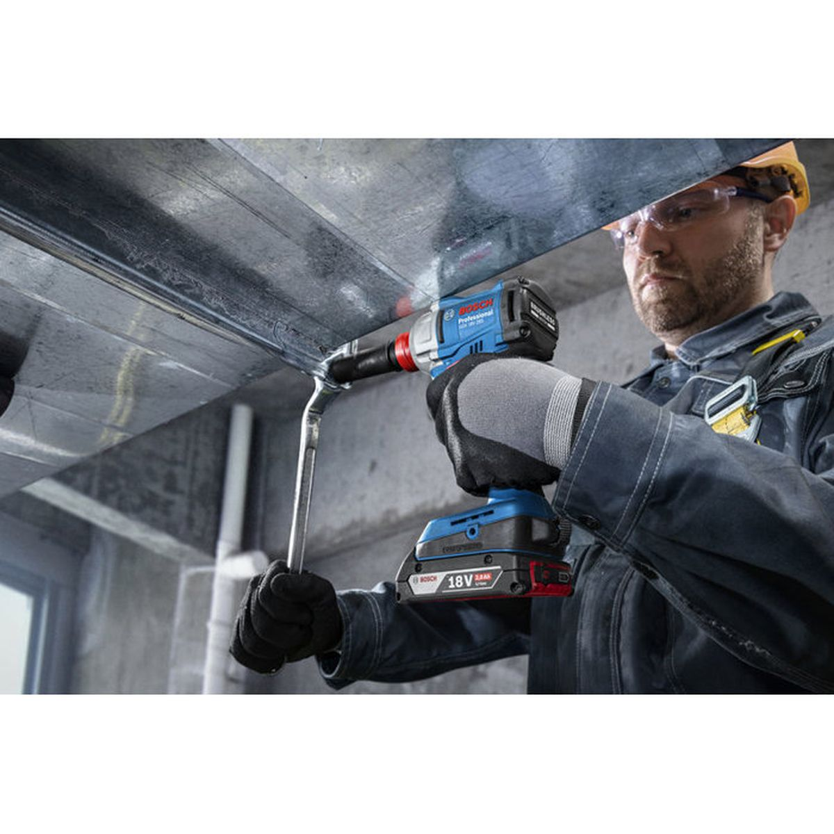 Handwerker mit Schutzbrille benutzt blauen Akku-Schrauber an Metallkonstruktion.