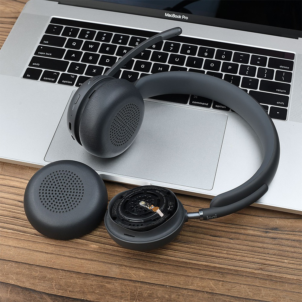 Ein schwarzes Wireless-Headset mit abnehmbarem Ohrpolster liegt auf Laptop-Tastatur und Holztisch.