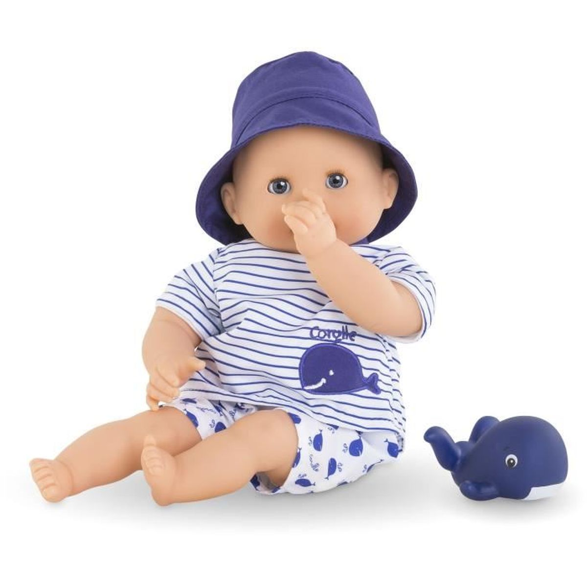 Eine Babypuppe mit blauem Hut und Wal-Outfit sitzt neben einem Wal-Spielzeug auf weißem Grund.
