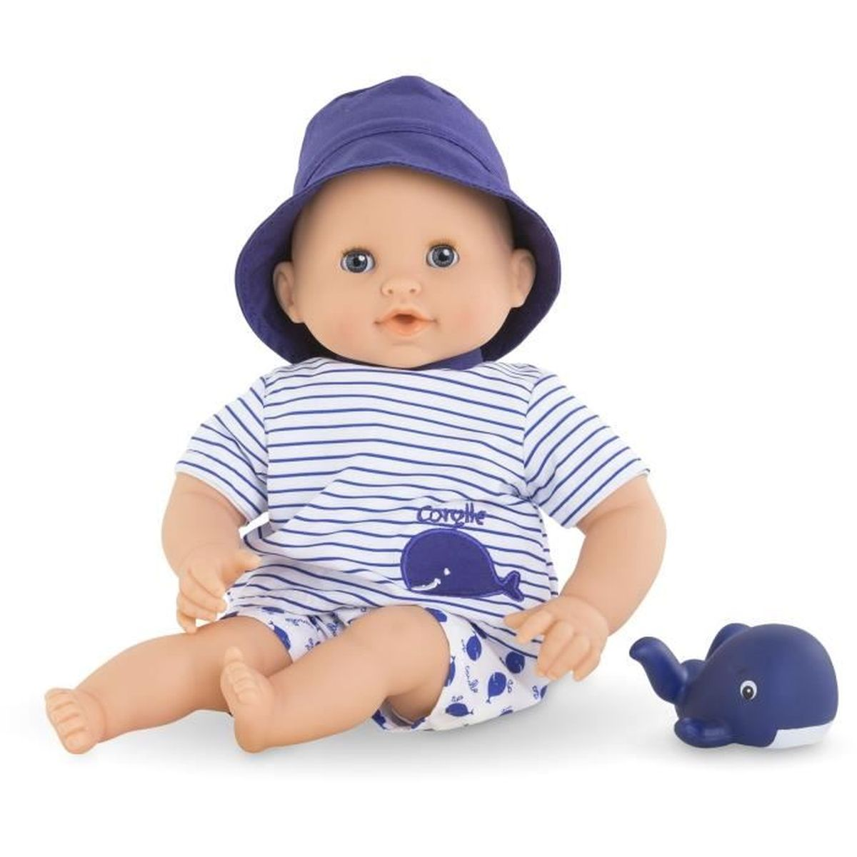 Eine Babypuppe mit blauem Hut, gestreiftem Shirt mit Walmotiv und passendem Spielzeugwal auf weißem Grund.