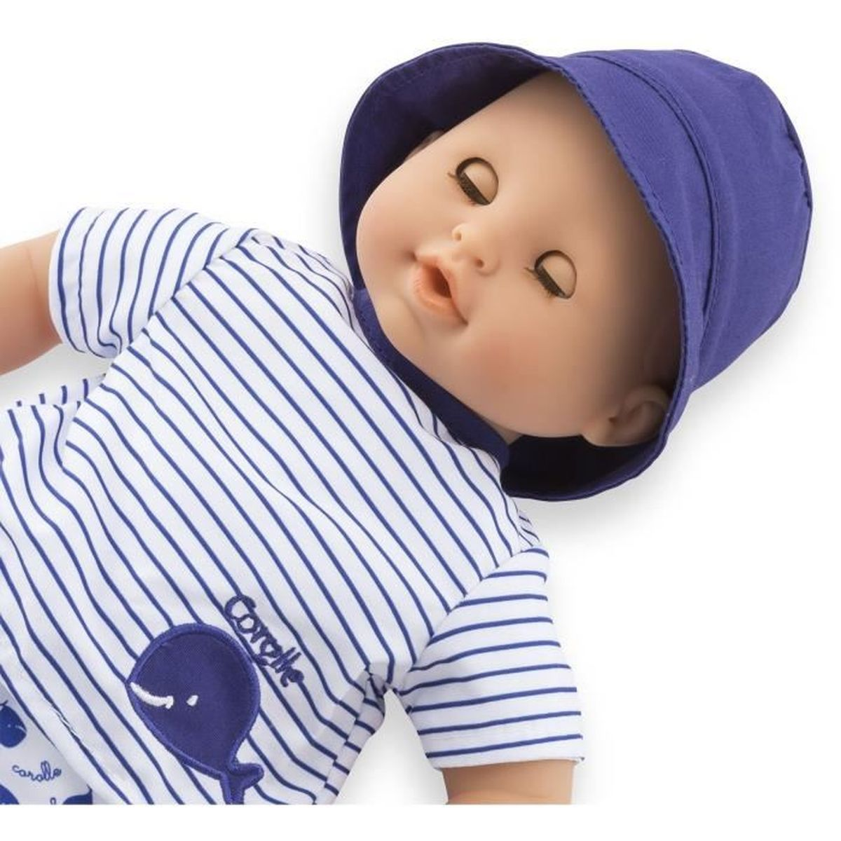 Eine Babypuppe mit blauem Sonnenhut und blau-weiß gestreiftem Shirt mit Wal-Motiv auf weißem Hintergrund.