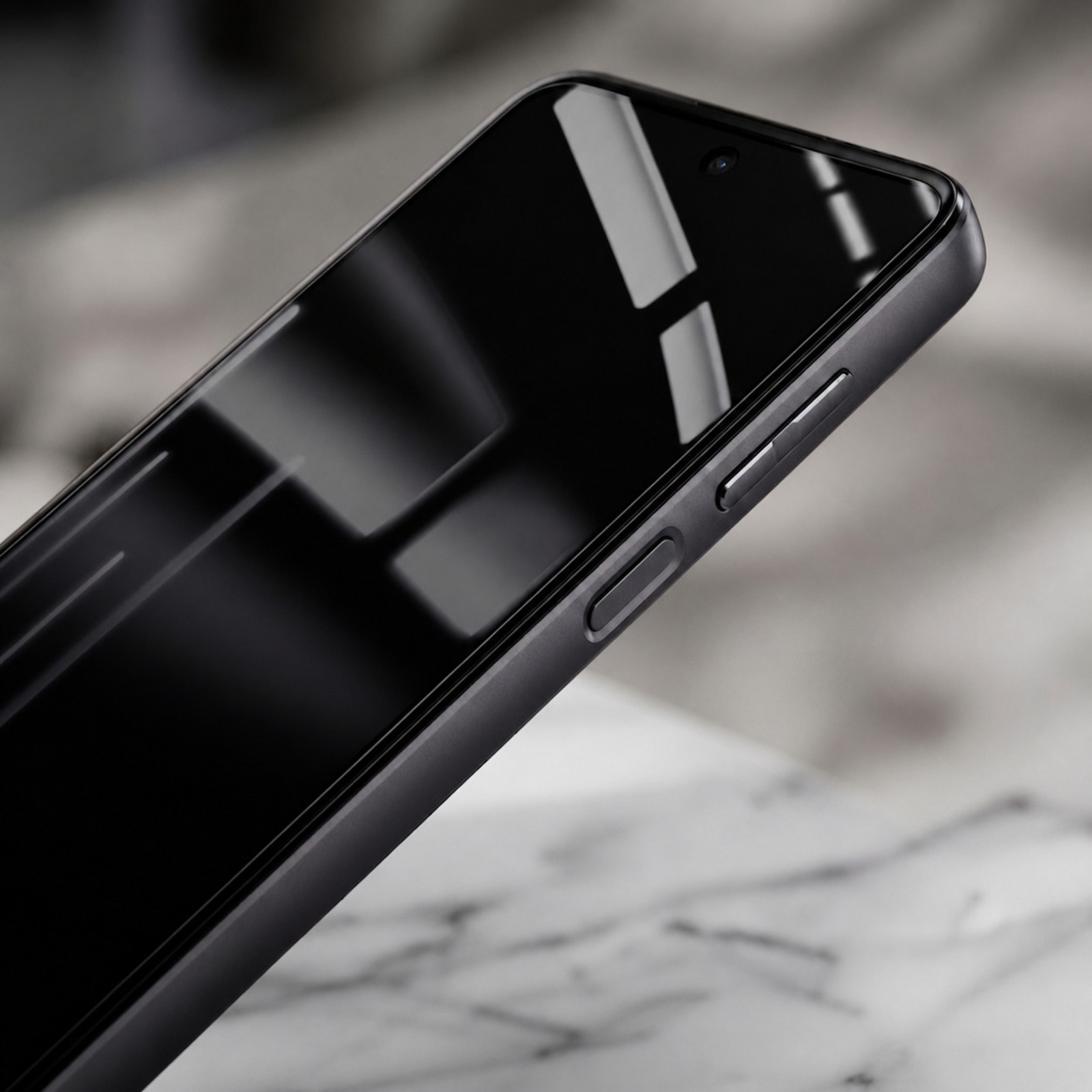 Uno smartphone nero con schermo riflettente poggiato in diagonale su una superficie di marmo.