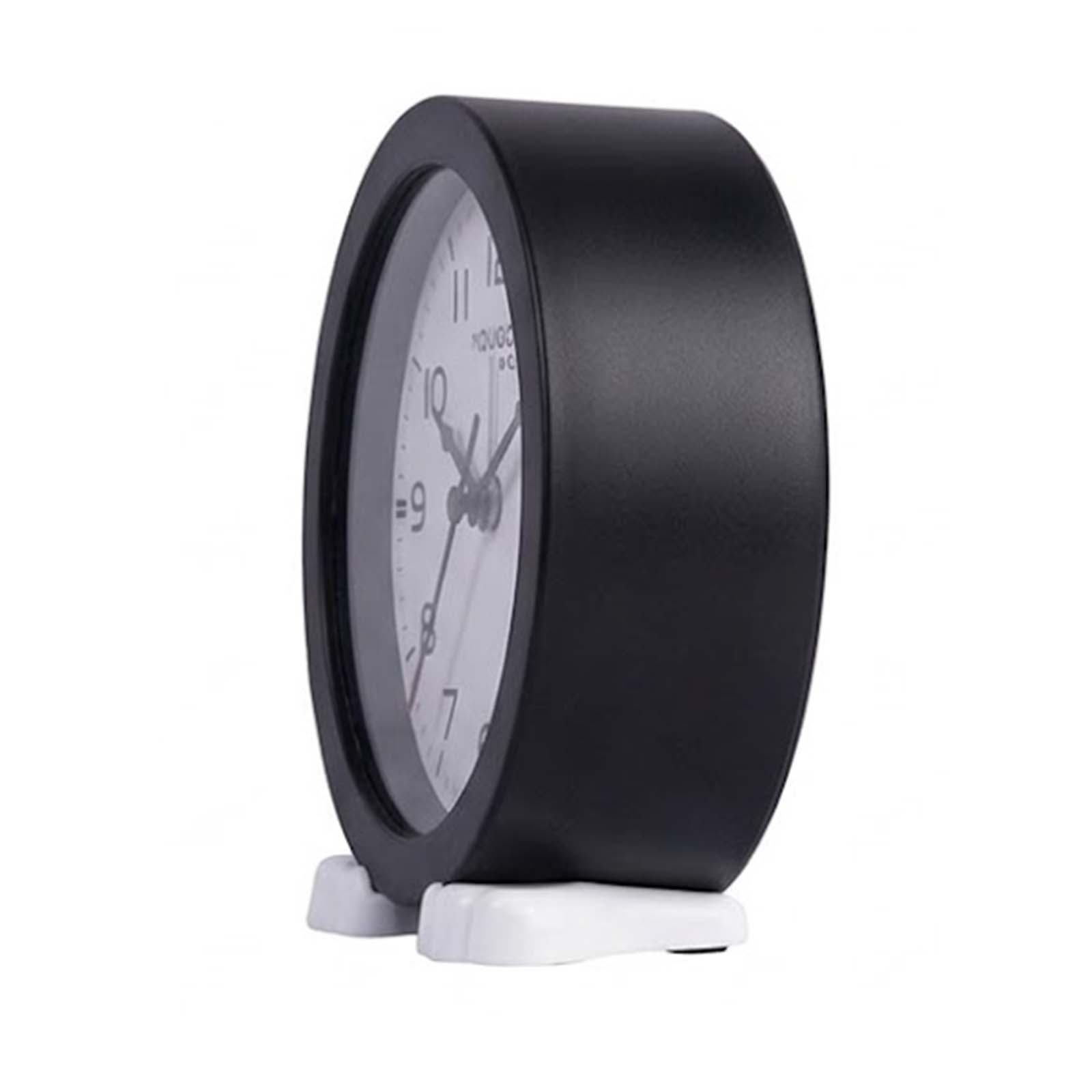 Un reloj de mesa negro con esfera blanca descansa sobre dos patas blancas sobre un fondo blanco.