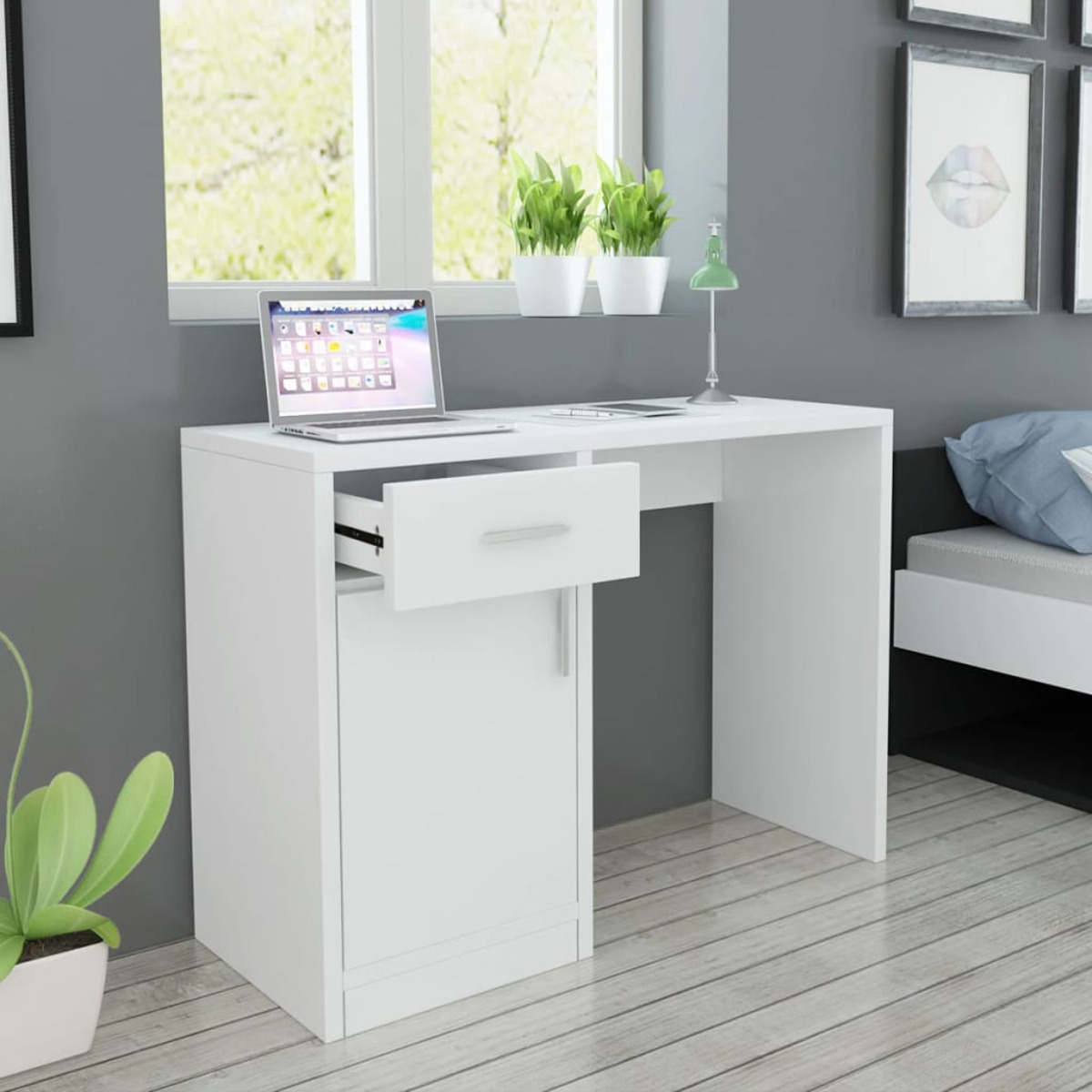 Ein weißer Schreibtisch mit offener Schublade, Laptop und grünen Pflanzen vor grauem Wandhintergrund.