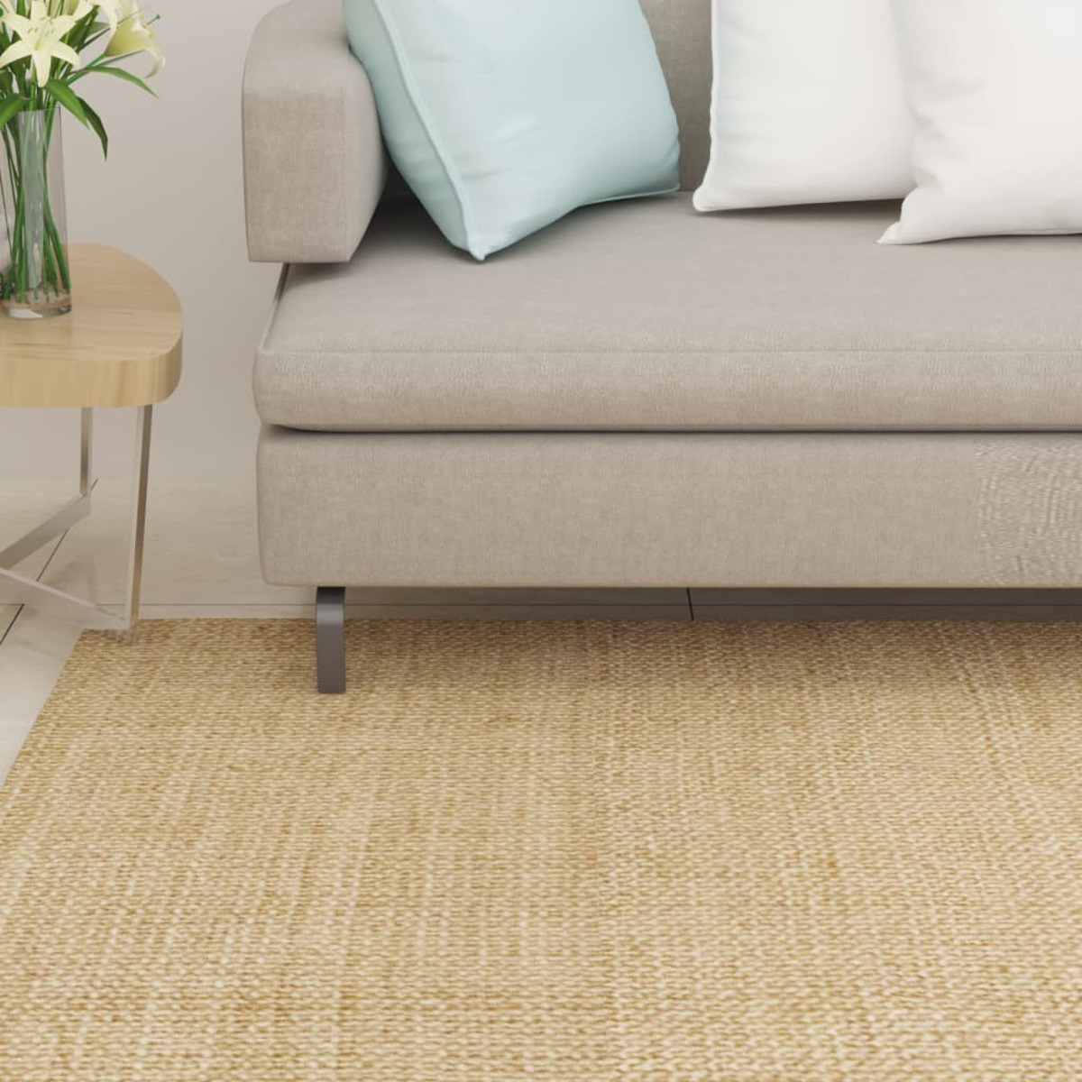 Ein graues Sofa mit Kissen steht auf einem beigen Teppich, daneben ein Holztisch mit Blumen.
