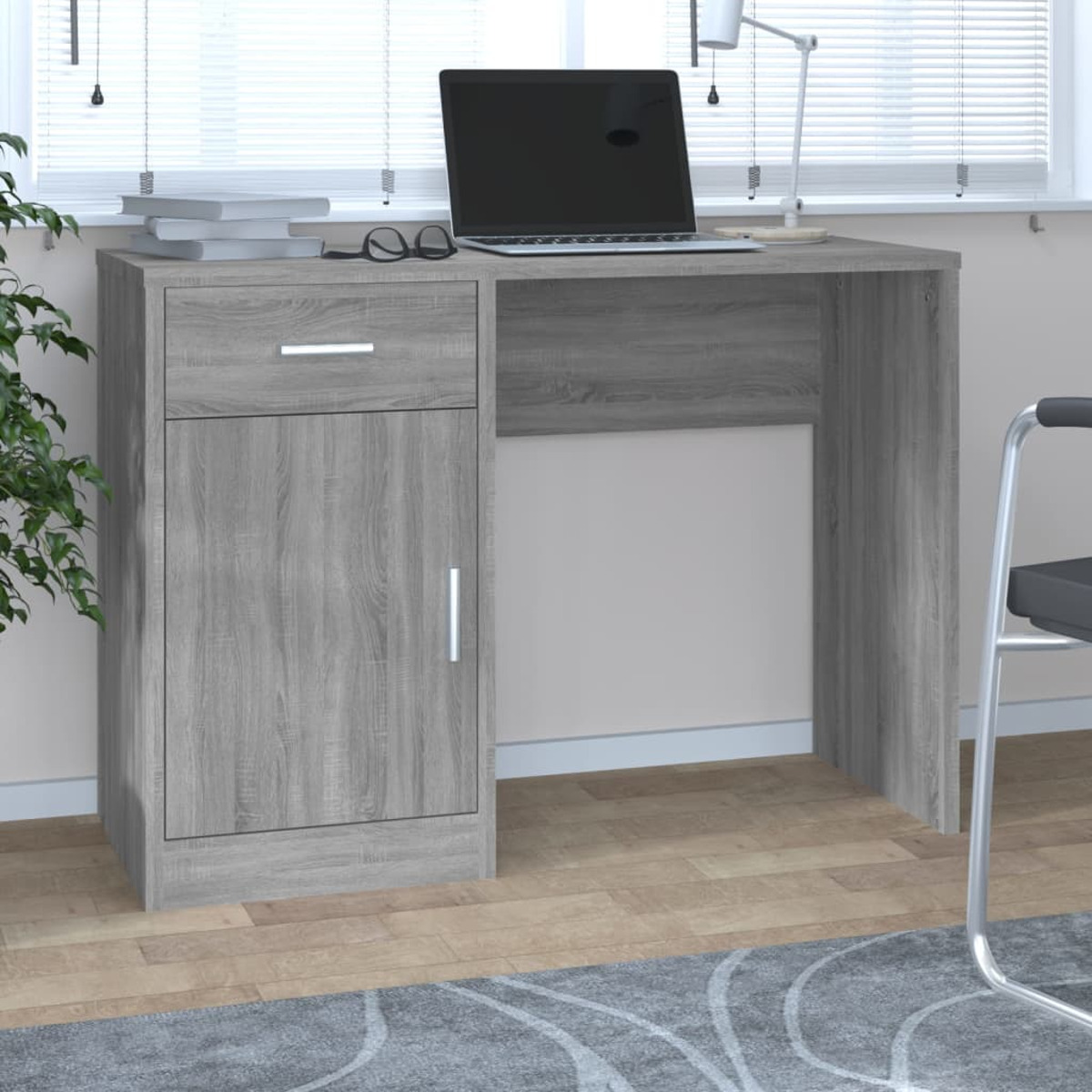 Ein grauer Holztisch mit Schublade, Schrank, Laptop, Brille und Büchern steht im Raum.