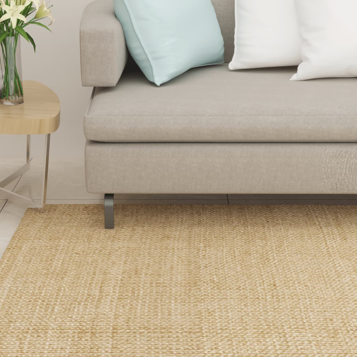 Ein graues Sofa mit Kissen steht über einem beigen Juteteppich, neben einem Holztisch mit Blumen.