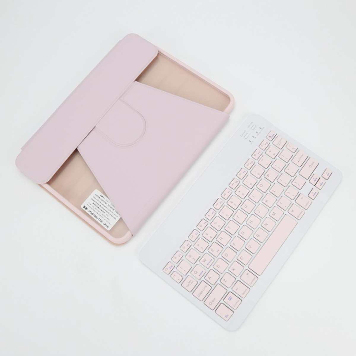 Una custodia rosa chiaro per tablet e una tastiera wireless bianca e rosa abbinata sono posizionate su una superficie bianca.