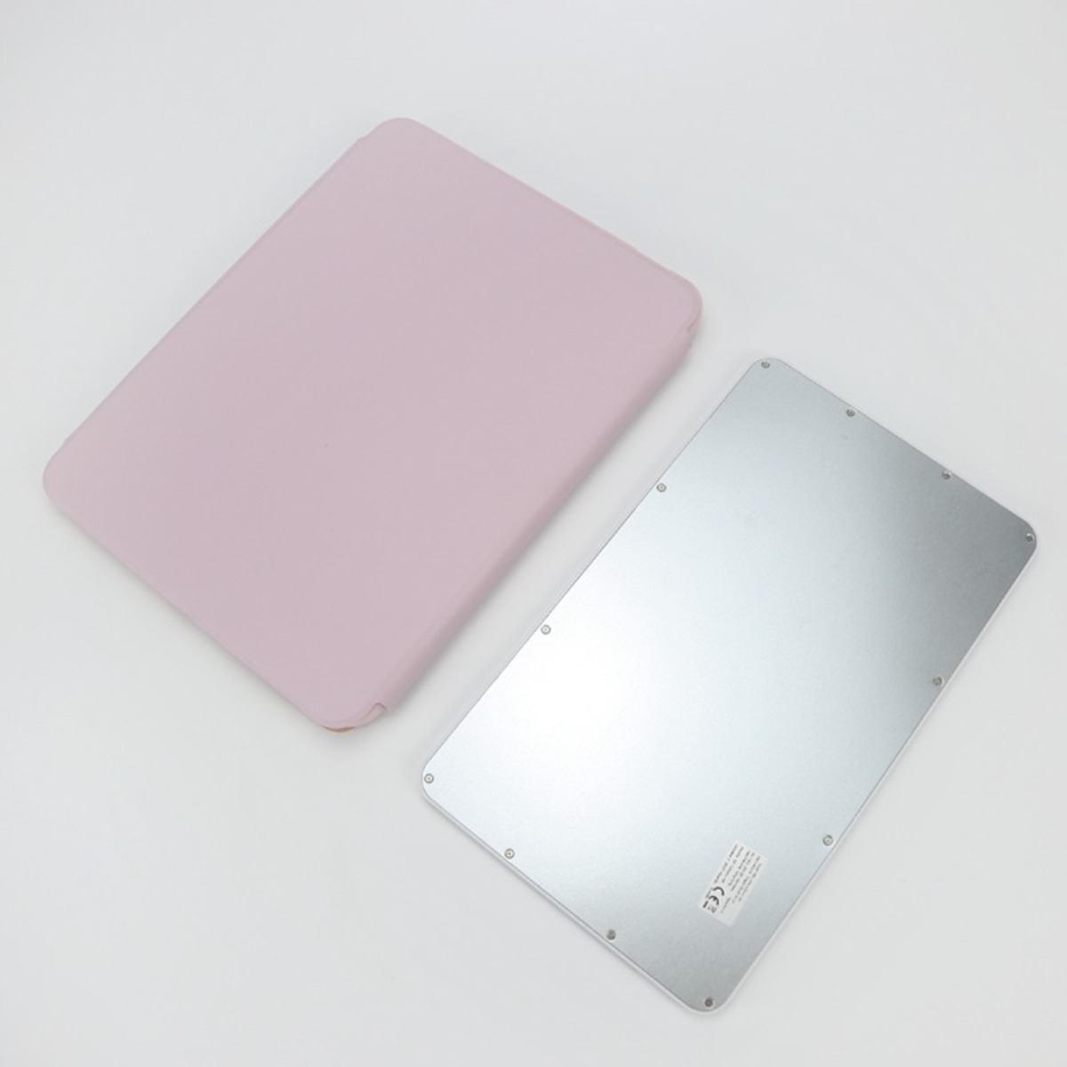 Un supporto per tablet rosa e una piastra metallica argentata giacciono piatti su un tavolo chiaro.