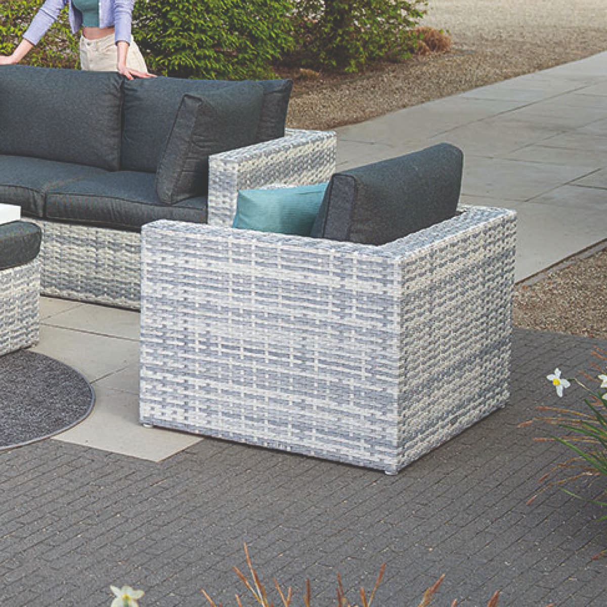 Grijs wicker tuinmeubilair met donkere kussens op een terras.