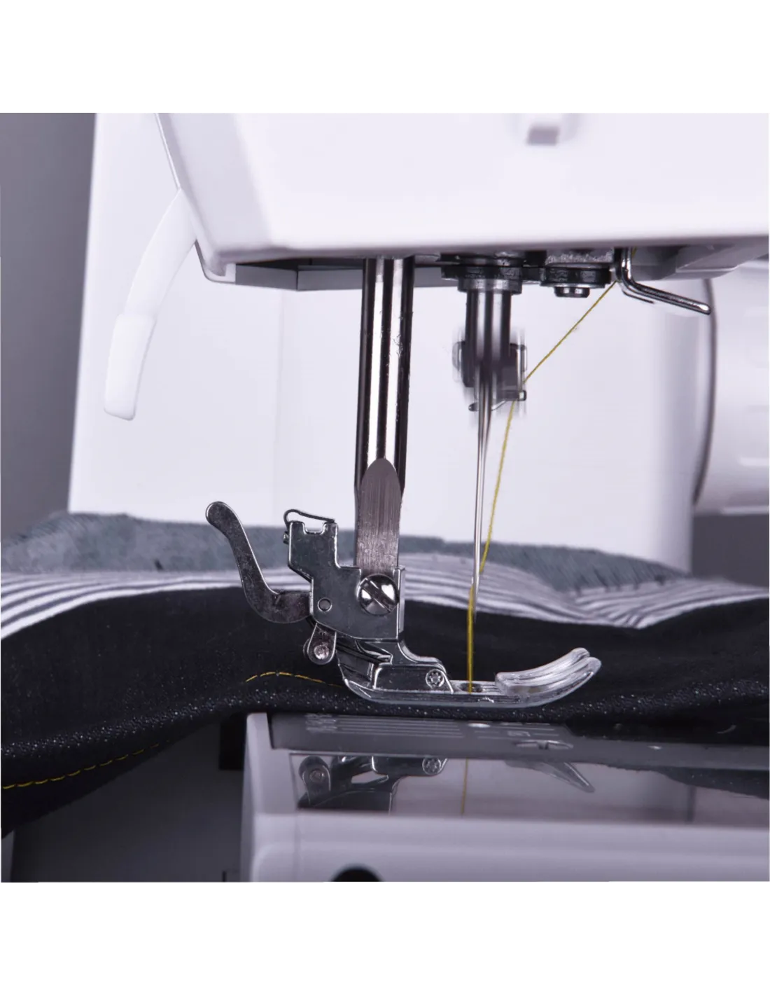 Close-up of a white sewing machine with a metal presser foot and yellow thread, stitching black fabric.