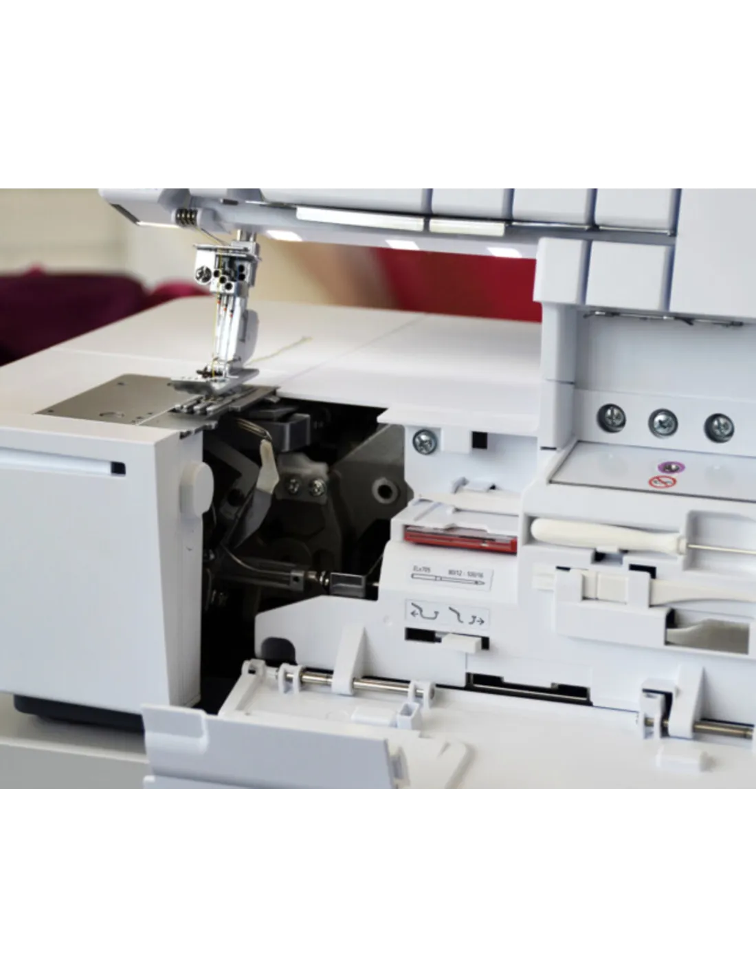 Close-up of a white overlock sewing machine with opened covers, showing inner mechanical parts.