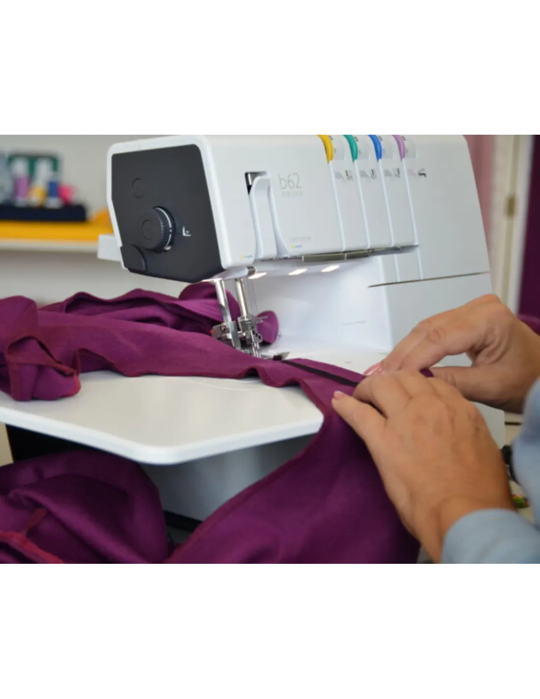 Hands guide purple fabric through a white overlock sewing machine.