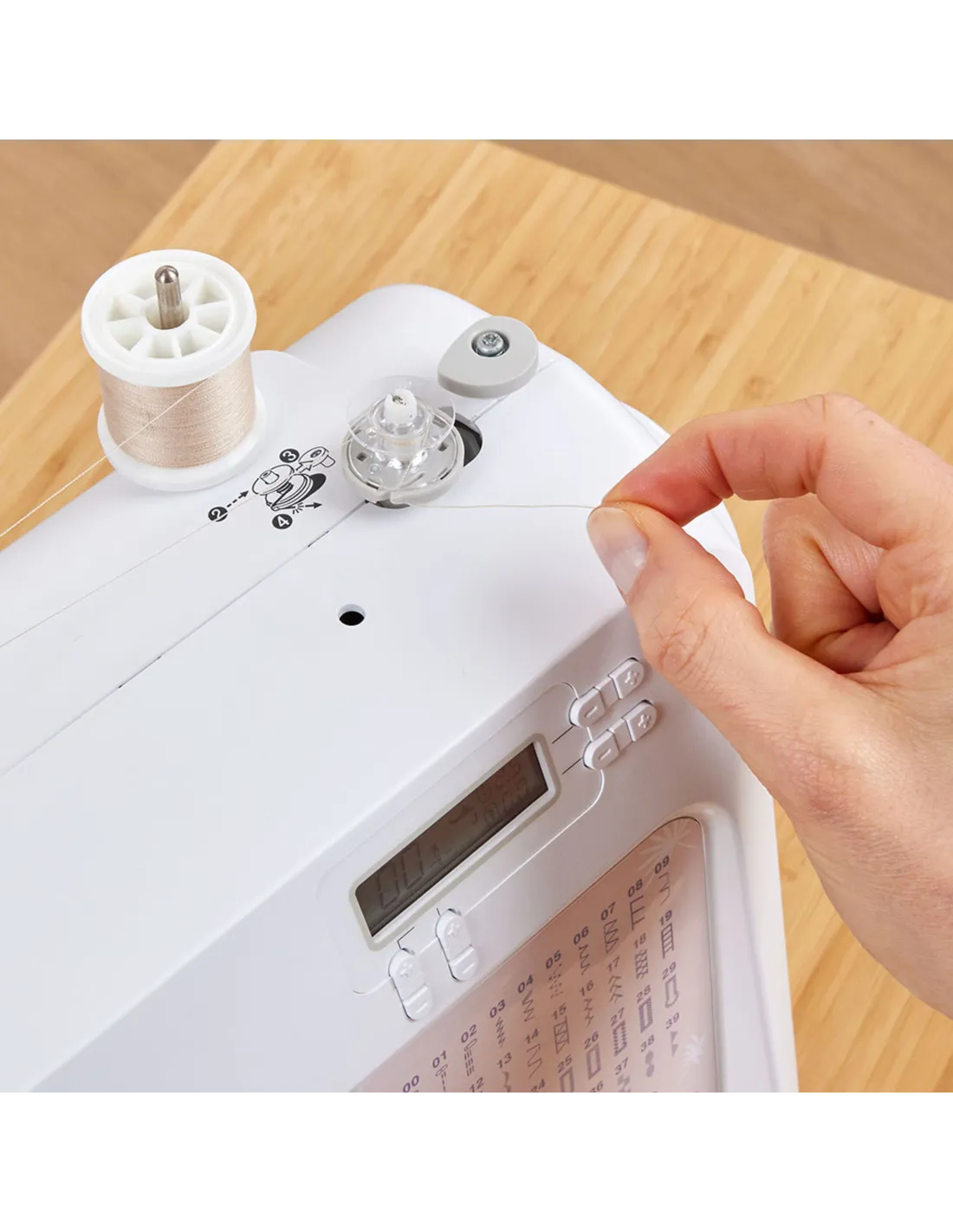 Eine Hand zieht Faden von einer Spule auf einer weißen Nähmaschine mit digitalem Display.