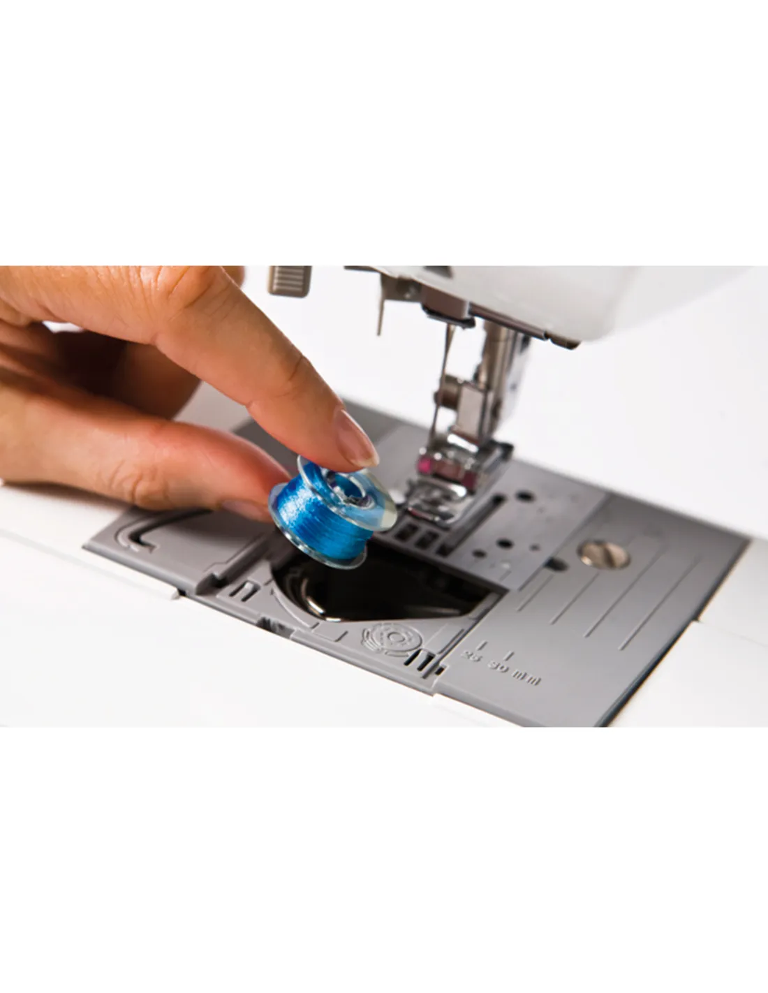 A hand placing a blue bobbin into a sewing machine.