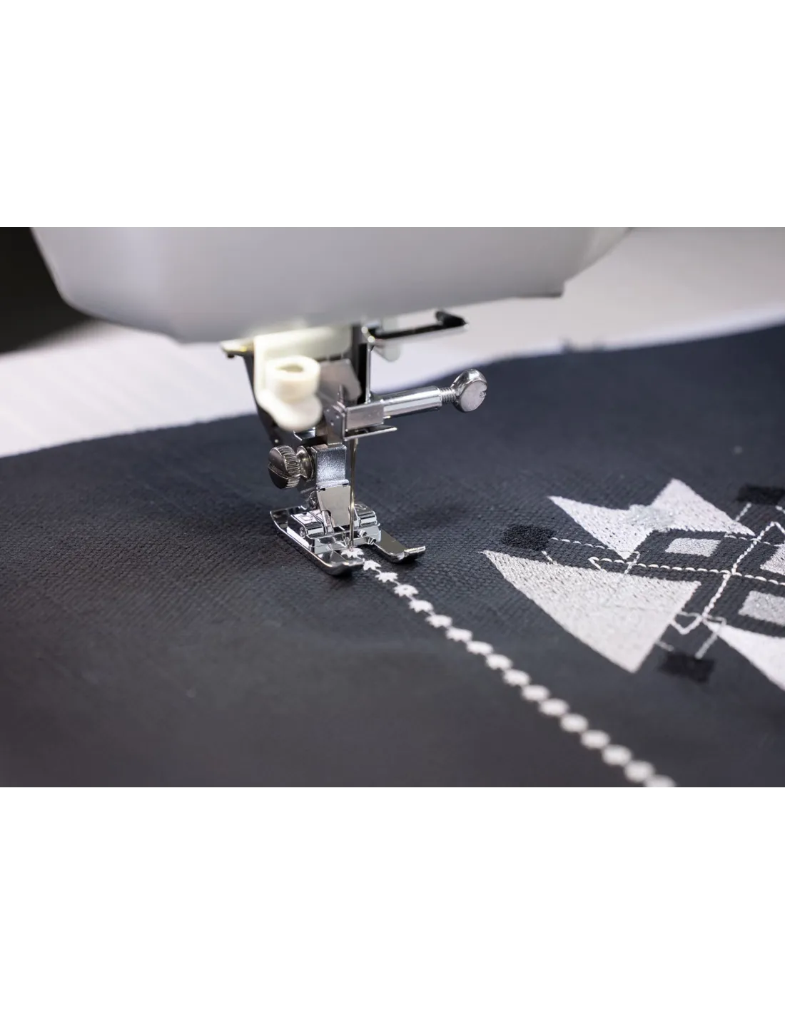 A sewing machine stitches white patterns onto dark blue fabric.