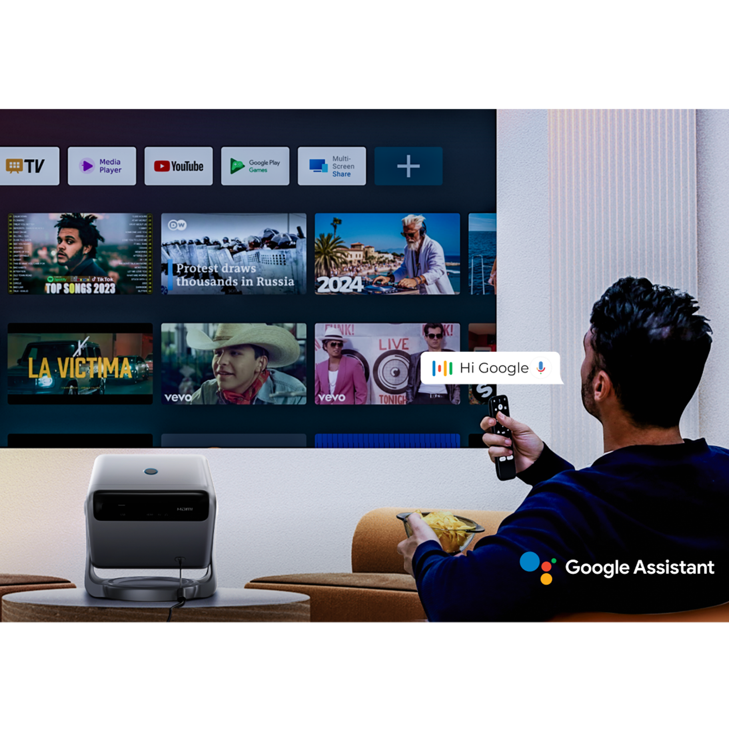 Ein Mann sitzt vor einer großen Leinwand, hält eine Fernbedienung und nutzt Google Assistant mit einem Projektor.