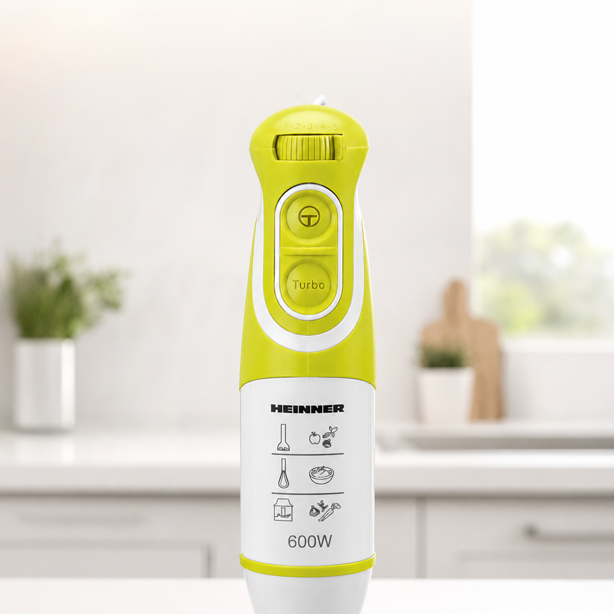 A green and white Heinner 600W hand blender stands on a kitchen counter.