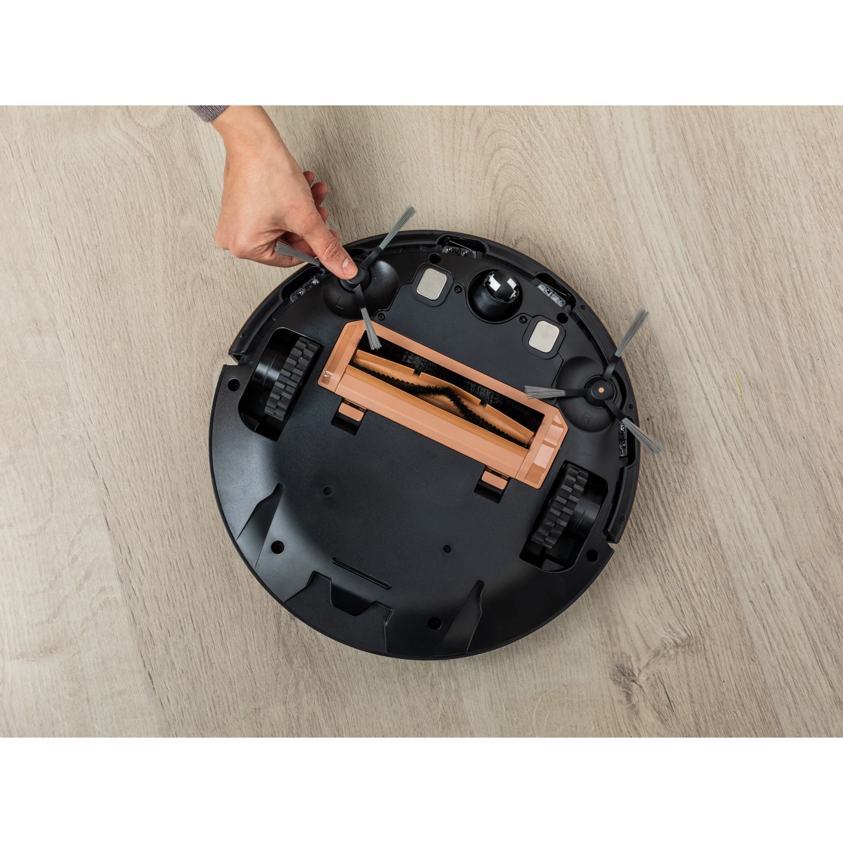 Una mano instala un cepillo lateral de repuesto en la parte inferior de un robot aspirador negro.