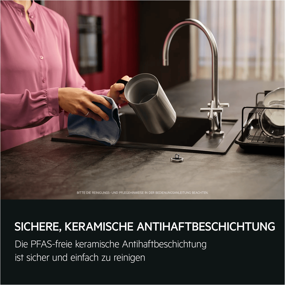 Eine Person im rosa Hemd wischt einen silbernen Topf in einer modernen Küche mit schwarzer Spüle sauber.