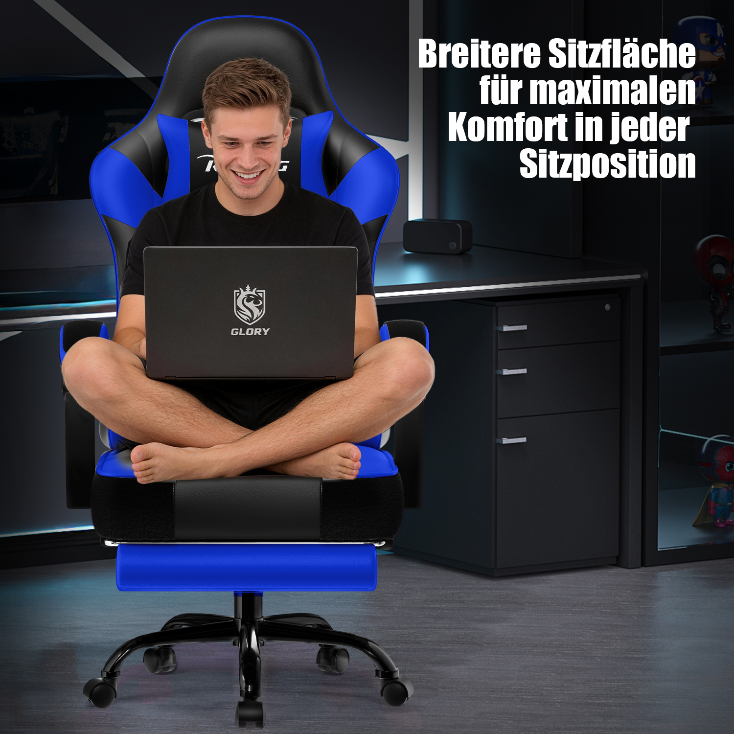 Ein Mann sitzt kreuzbeinig mit Laptop in einem blauschwarzen Gaming-Stuhl vor einem Schreibtisch.