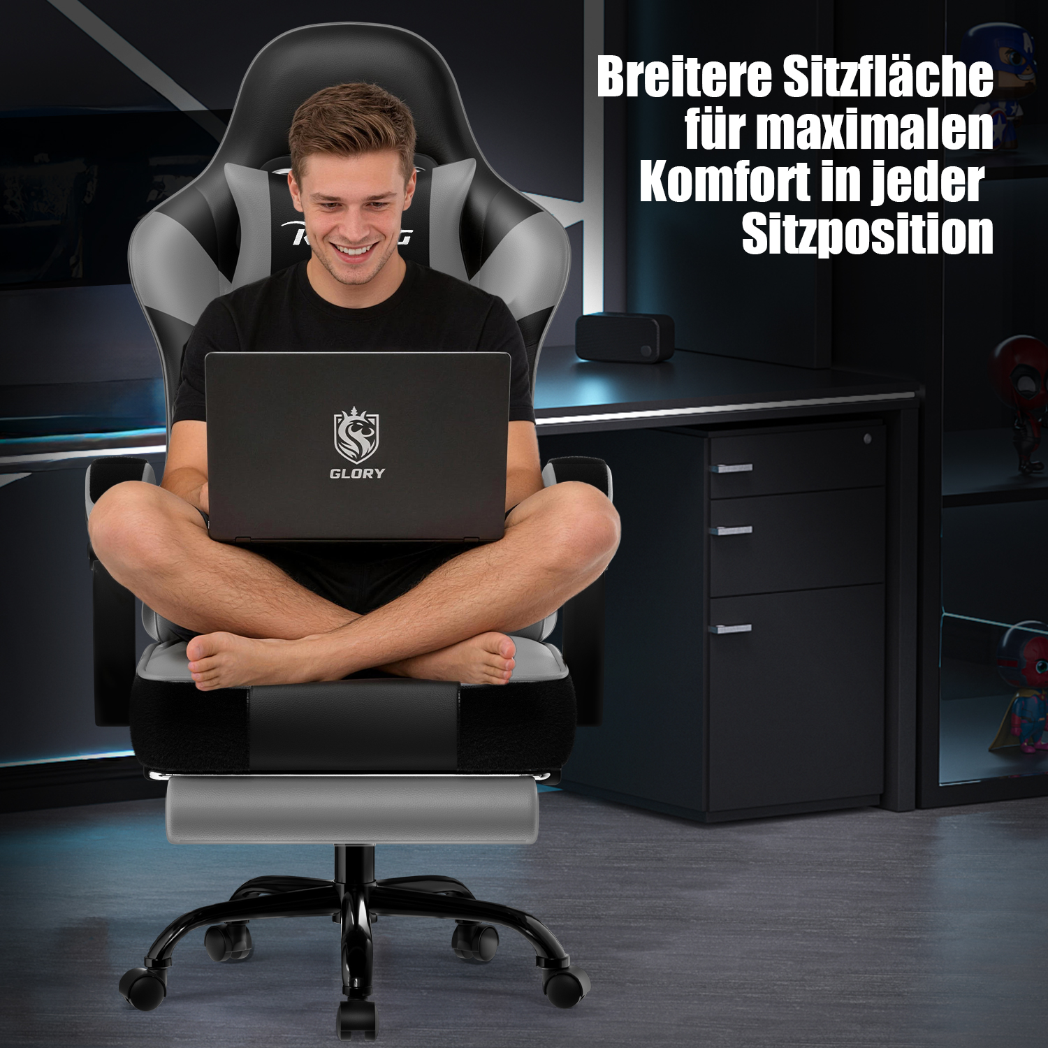 Mann sitzt mit gekreuzten Beinen auf einem breiten grauen Gaming-Stuhl und nutzt einen Laptop.