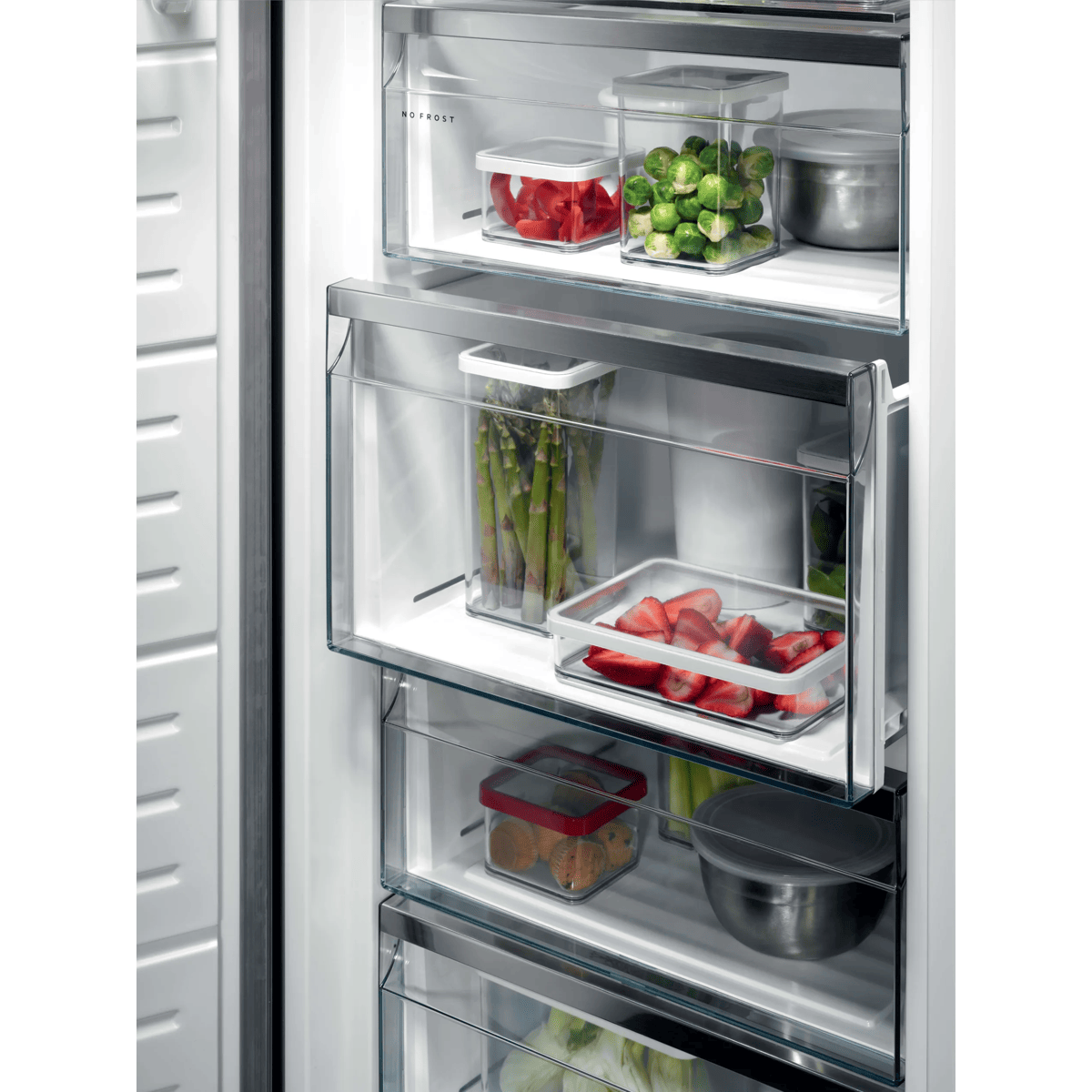 Cajones de congelador abiertos con recipientes transparentes llenos de verduras y fresas.
