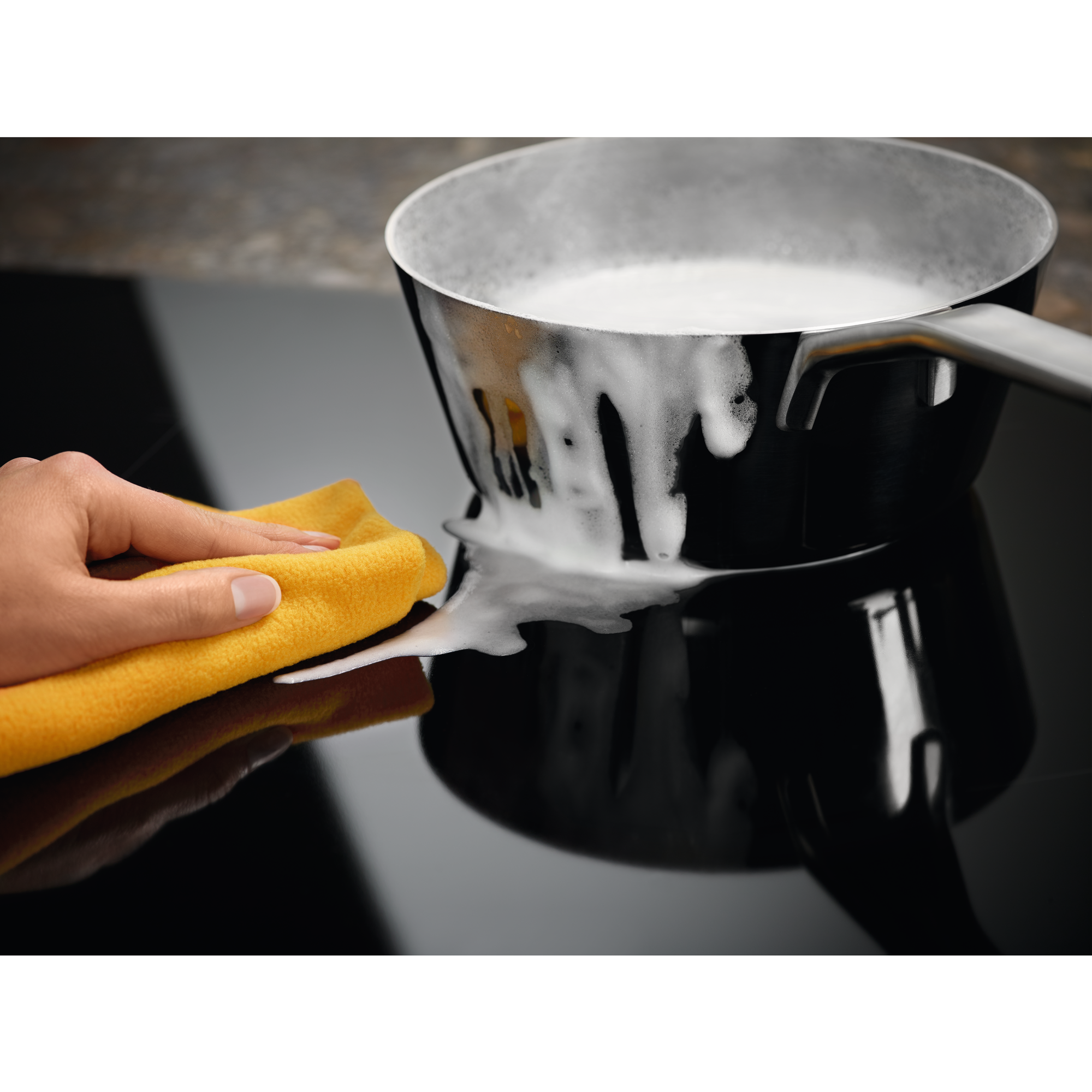 Una mano usa un paño amarillo para limpiar espuma de una placa negra.
