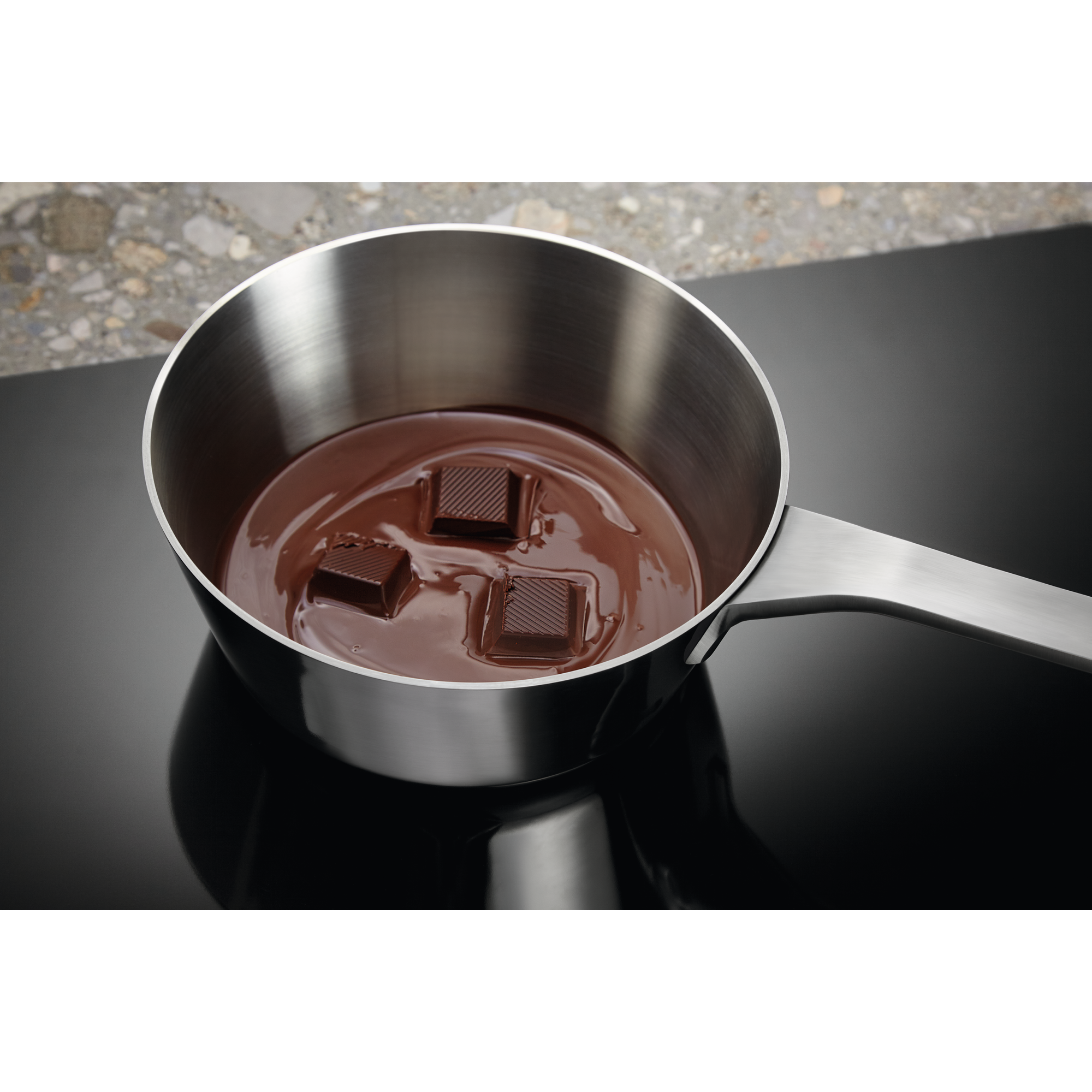 Trozo de chocolate derritiéndose en una pequeña cacerola de acero inoxidable en una estufa oscura.