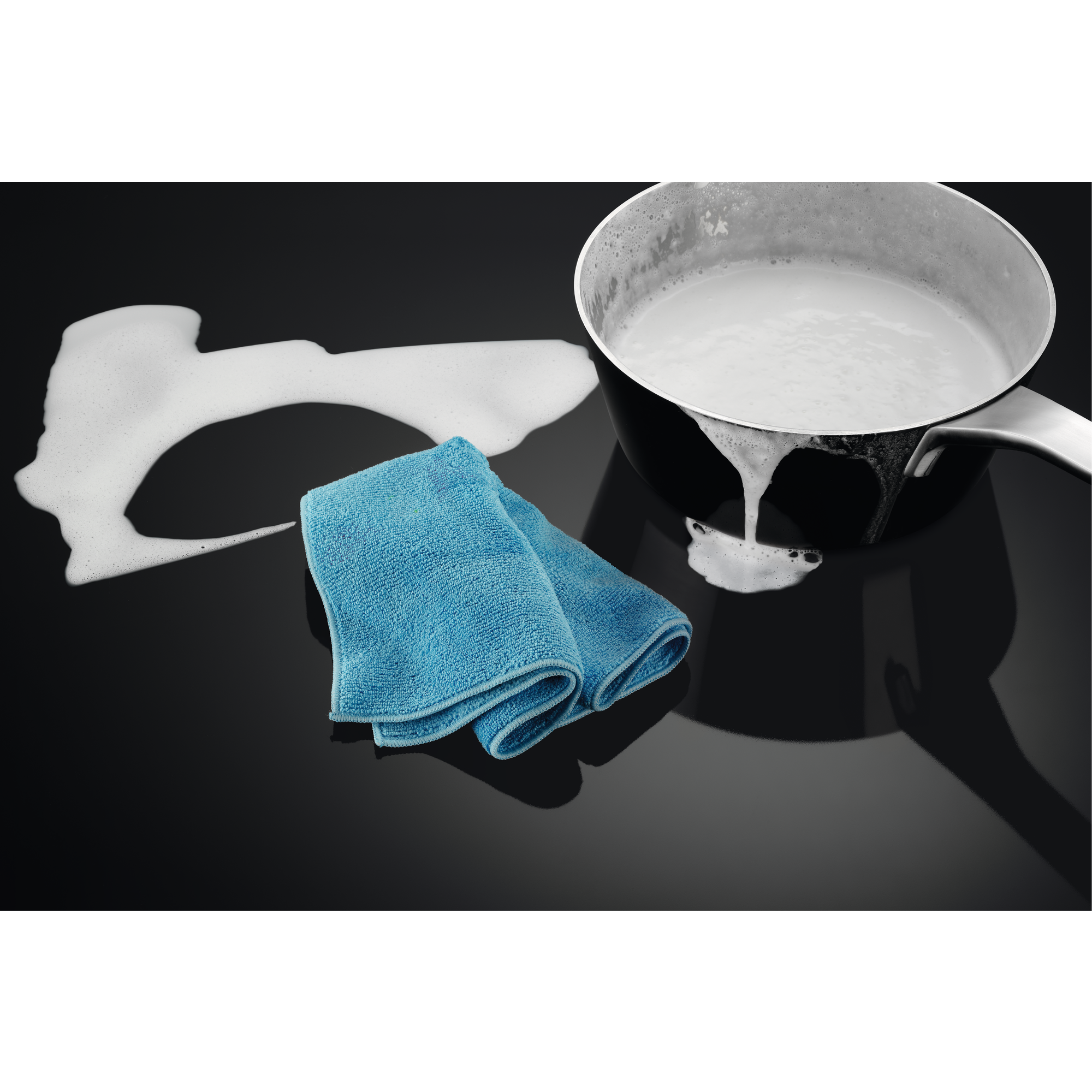 Un trapo azul, espuma de jabón y una olla en una superficie negra.