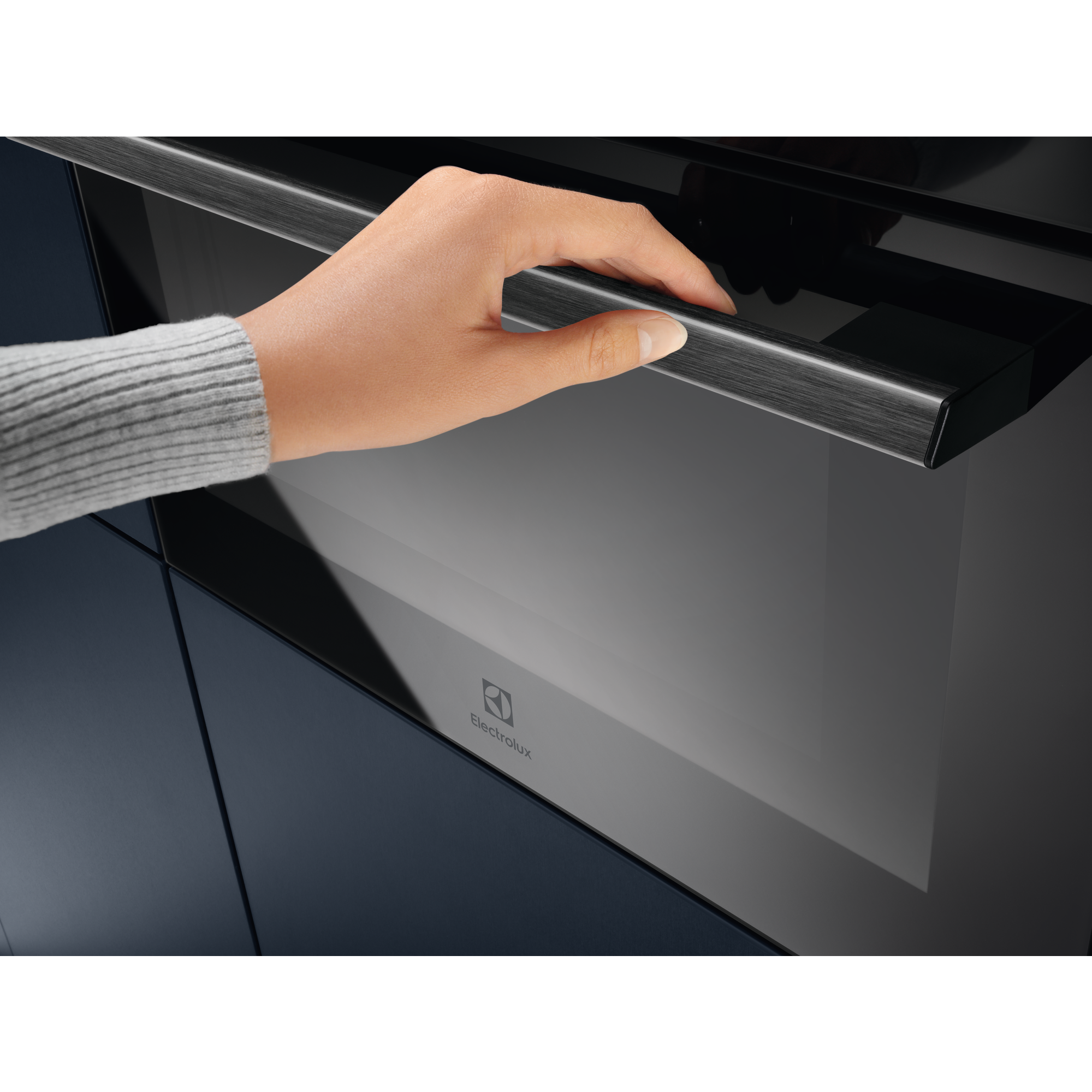 Una mano abre la manija plateada de un horno Electrolux negro moderno.