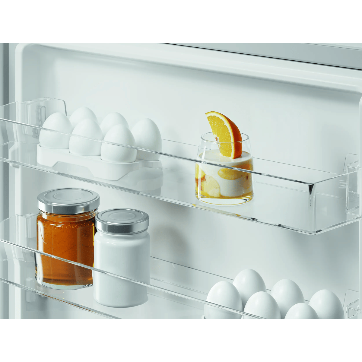 Puerta de refrigerador con huevos, tarros, yogur y rodaja de naranja.