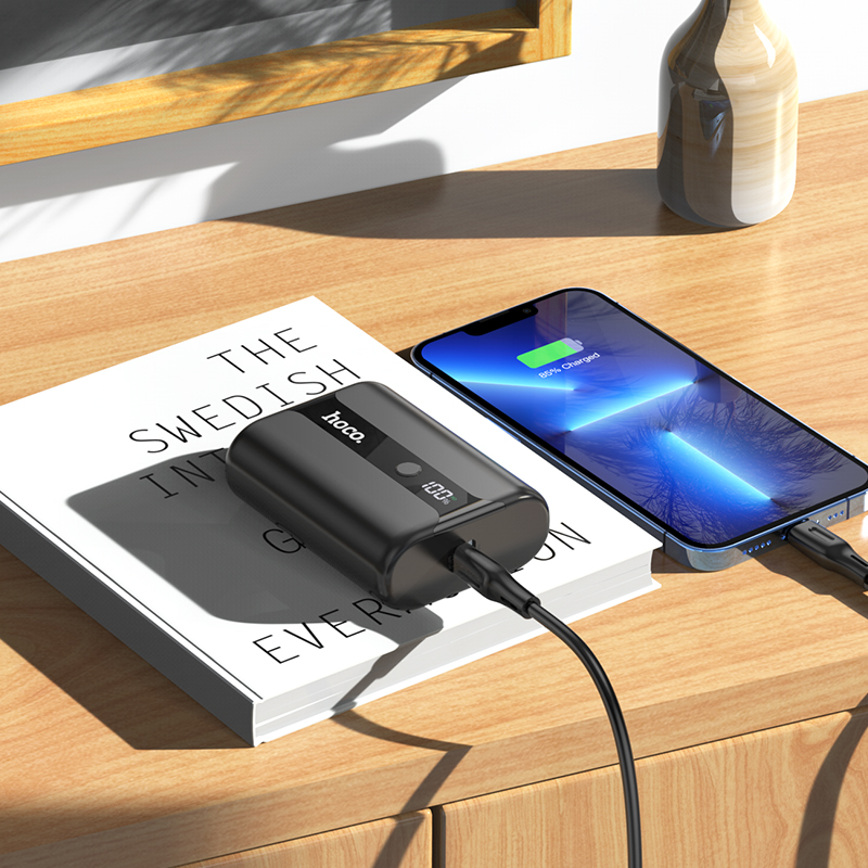 Un banco de energía sobre un libro en una mesa de madera, conectado a un teléfono.