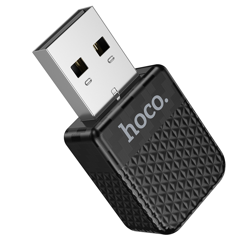 Un pequeño adaptador USB hoco negro con superficie texturizada y un conector USB plateado sobre fondo blanco.