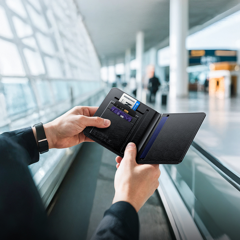 Persona sosteniendo una billetera de viaje negra con tarjetas en un aeropuerto brillante y borroso.