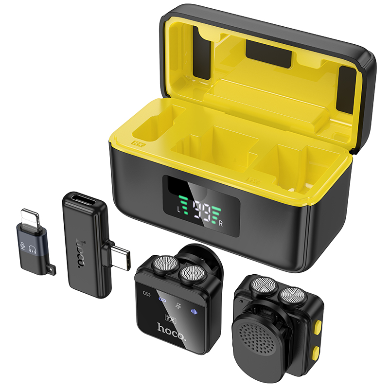 Estuche de carga negro con interior amarillo, dos micrófonos compactos y dos adaptadores sobre fondo blanco.