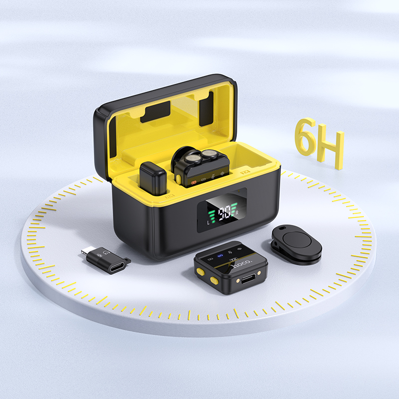Estuche de carga negro con interior amarillo, dos pequeños transmisores de audio, clip y adaptador en plataforma redonda.