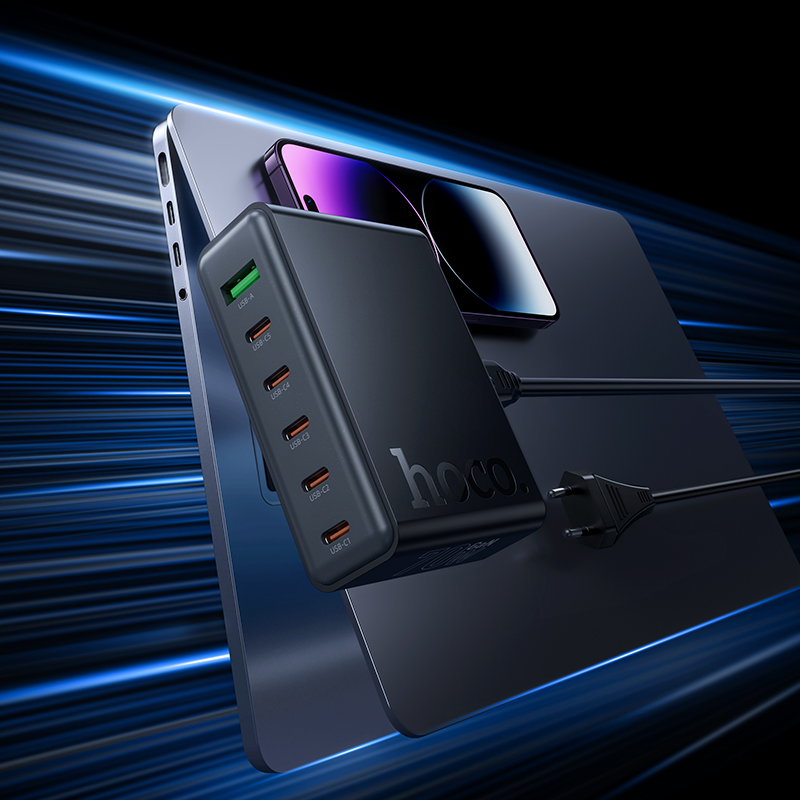 Un cargador USB múltiple Hoco negro sobre un portátil con un smartphone, con fondo de luz azul.