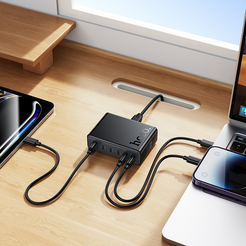 Un concentrador USB-C negro en un escritorio de madera, conectado a una computadora portátil, tableta y teléfono inteligente.