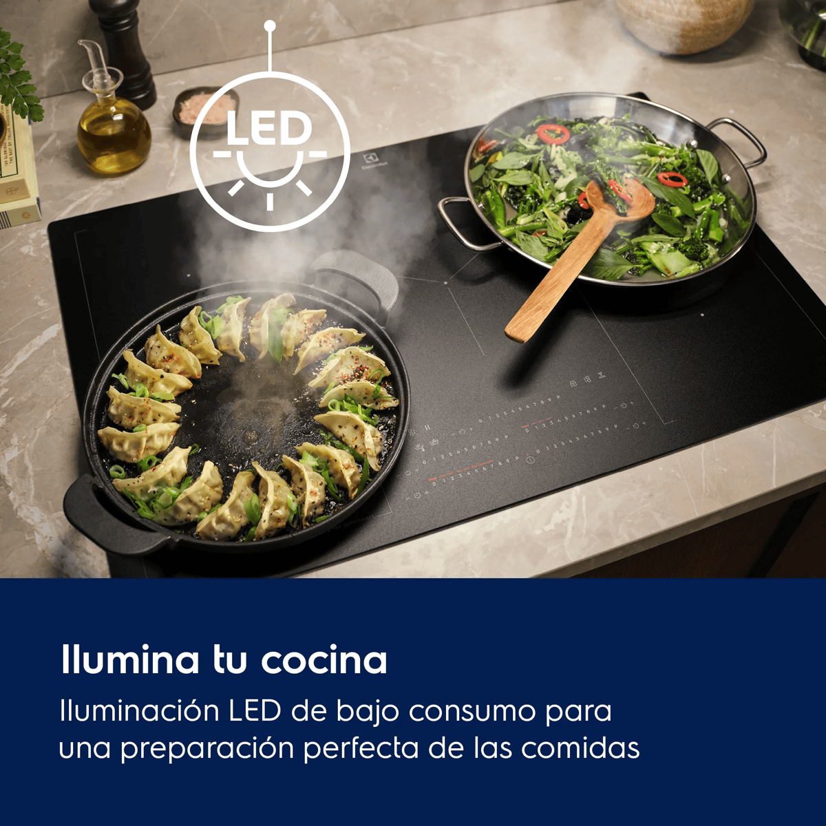 Una placa de inducción negra con dos sartenes: una con empanadillas fritas y otra con verduras verdes.