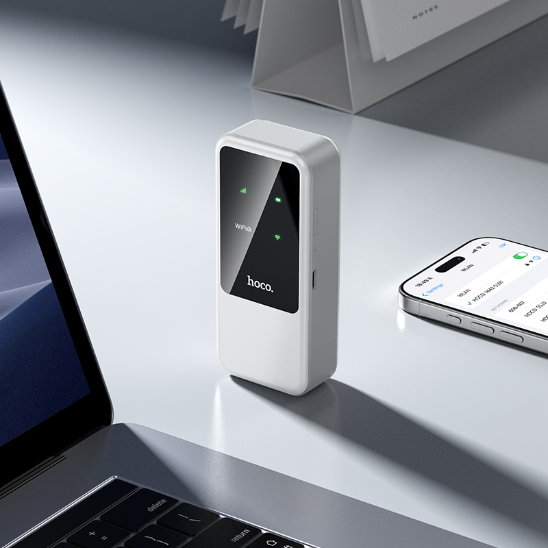 Un dispositivo Hoco blanco está en un escritorio junto a un portátil y un smartphone.