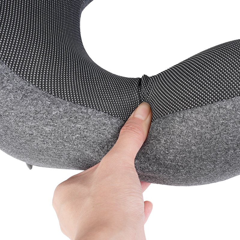 Una mano presionando una almohada de viaje gris en forma de U con malla negra.