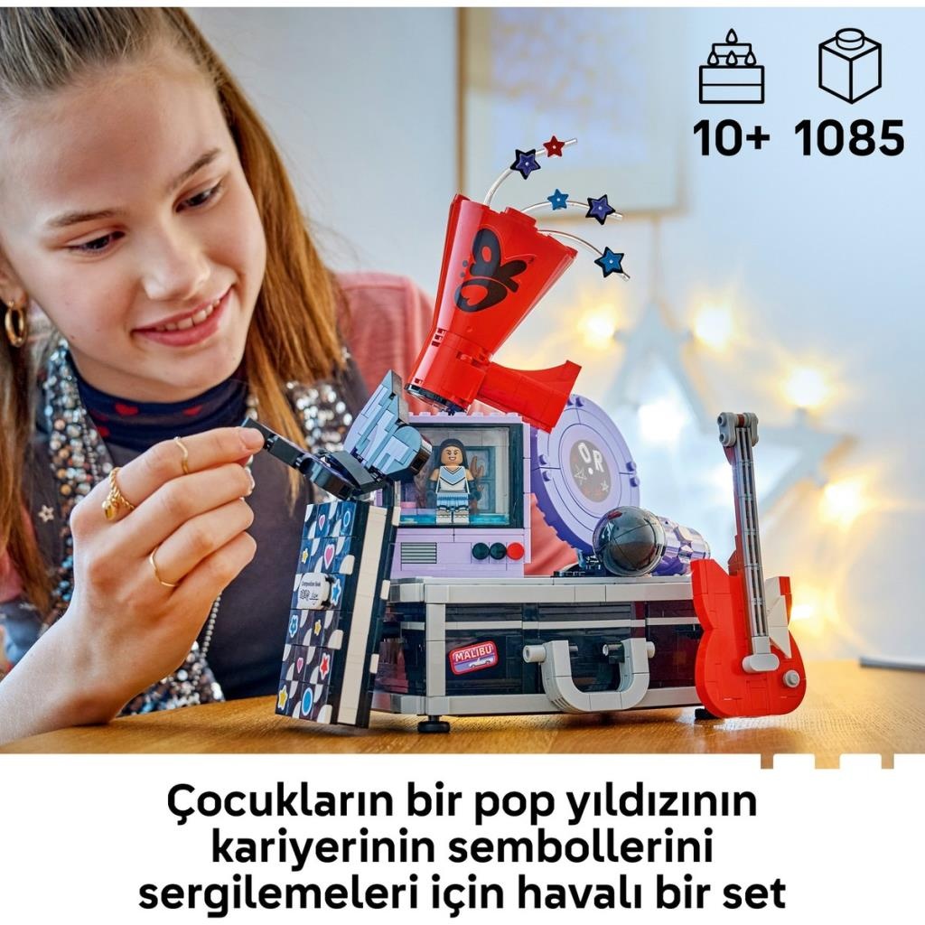 Genç bir kız ahşap masada megafon, gitar ve dekoratif semboller içeren renkli bir Lego seti kuruyor.