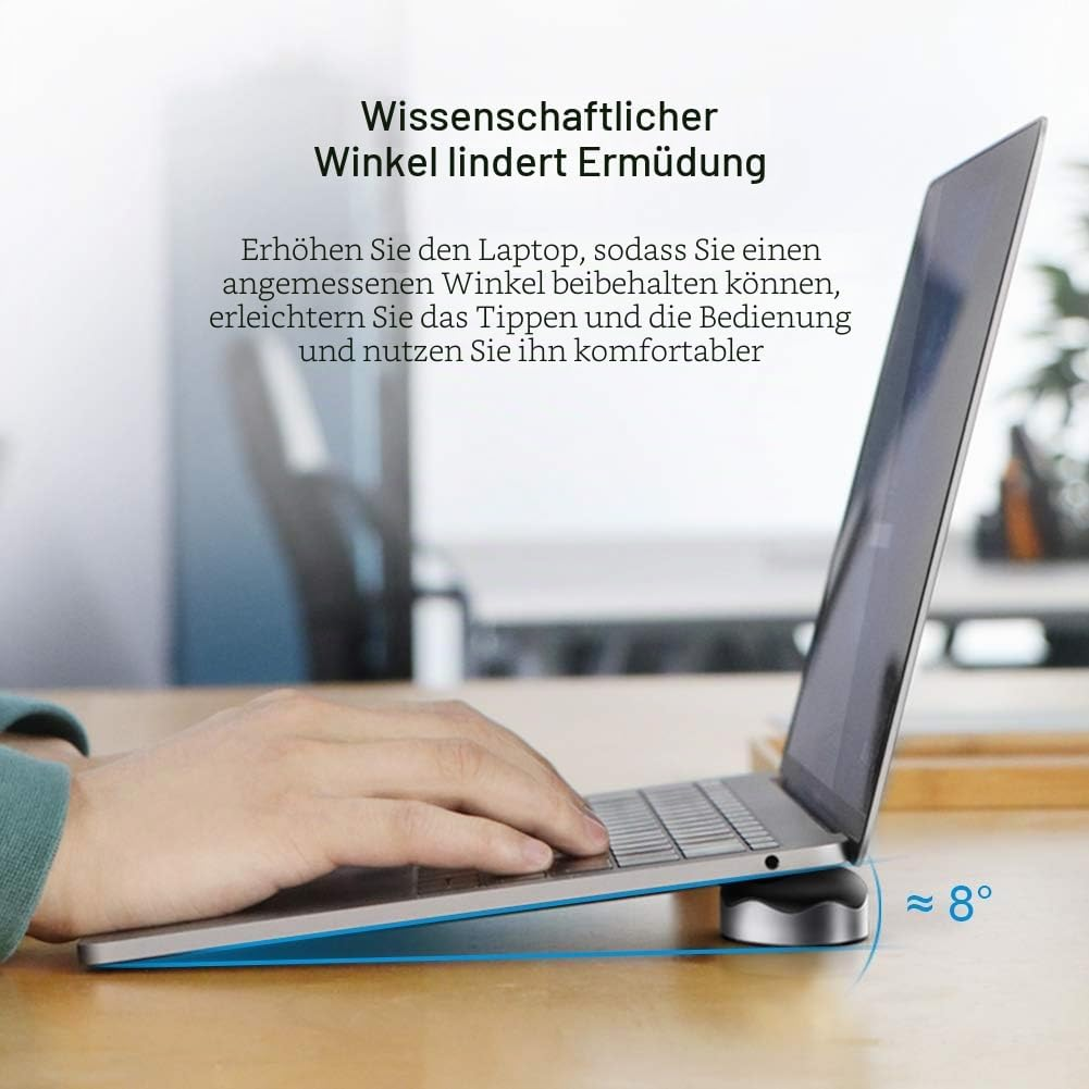 Ein Laptop steht auf einem Schreibtisch, leicht geneigt durch einen kleinen Ständer.