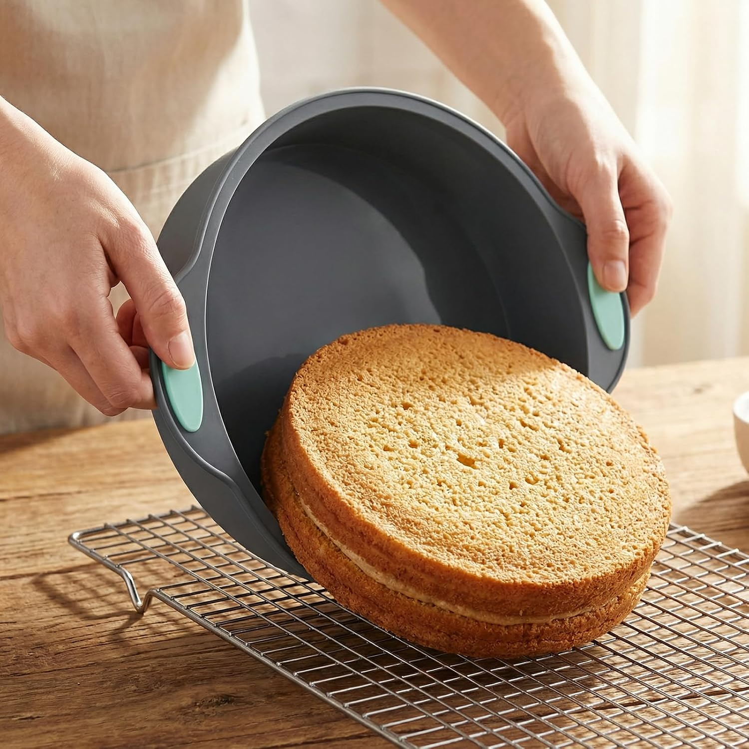 Person nimmt gebackenen Kuchen aus einer grauen Silikonbackform auf ein Gitter.