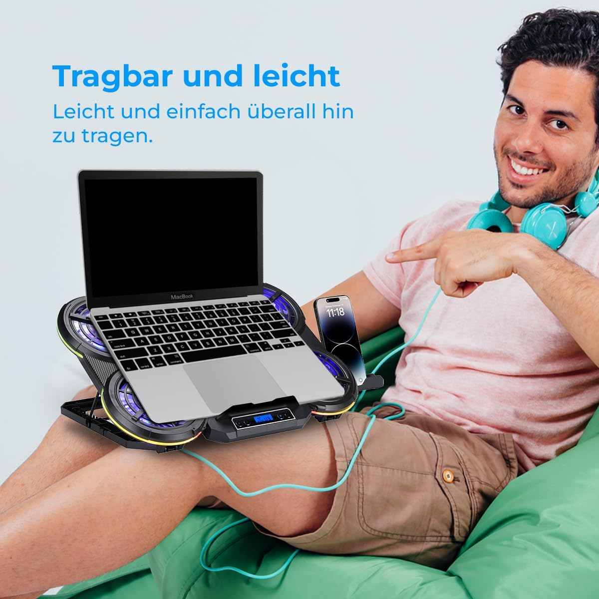 Mann sitzt auf einem grünen Kissen und zeigt auf einen Laptop auf einem Kühlerständer.