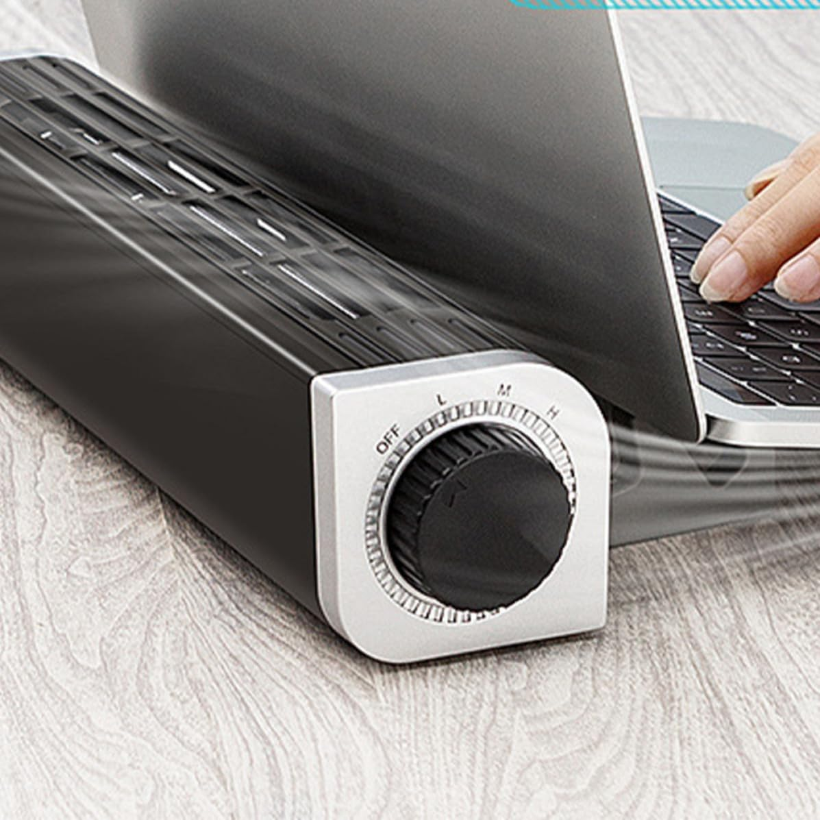 Ein tragbarer schwarzer Ventilator mit Drehregler steht auf einem Holztisch neben einem Laptop.