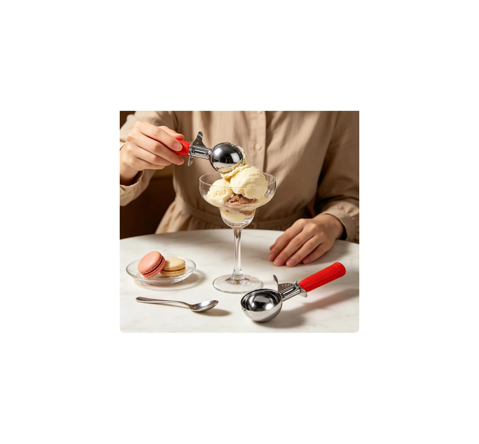 Eine Person schöpft Eis in einen Glasbecher auf einem weißen Tisch mit Makronen und einem Löffel.