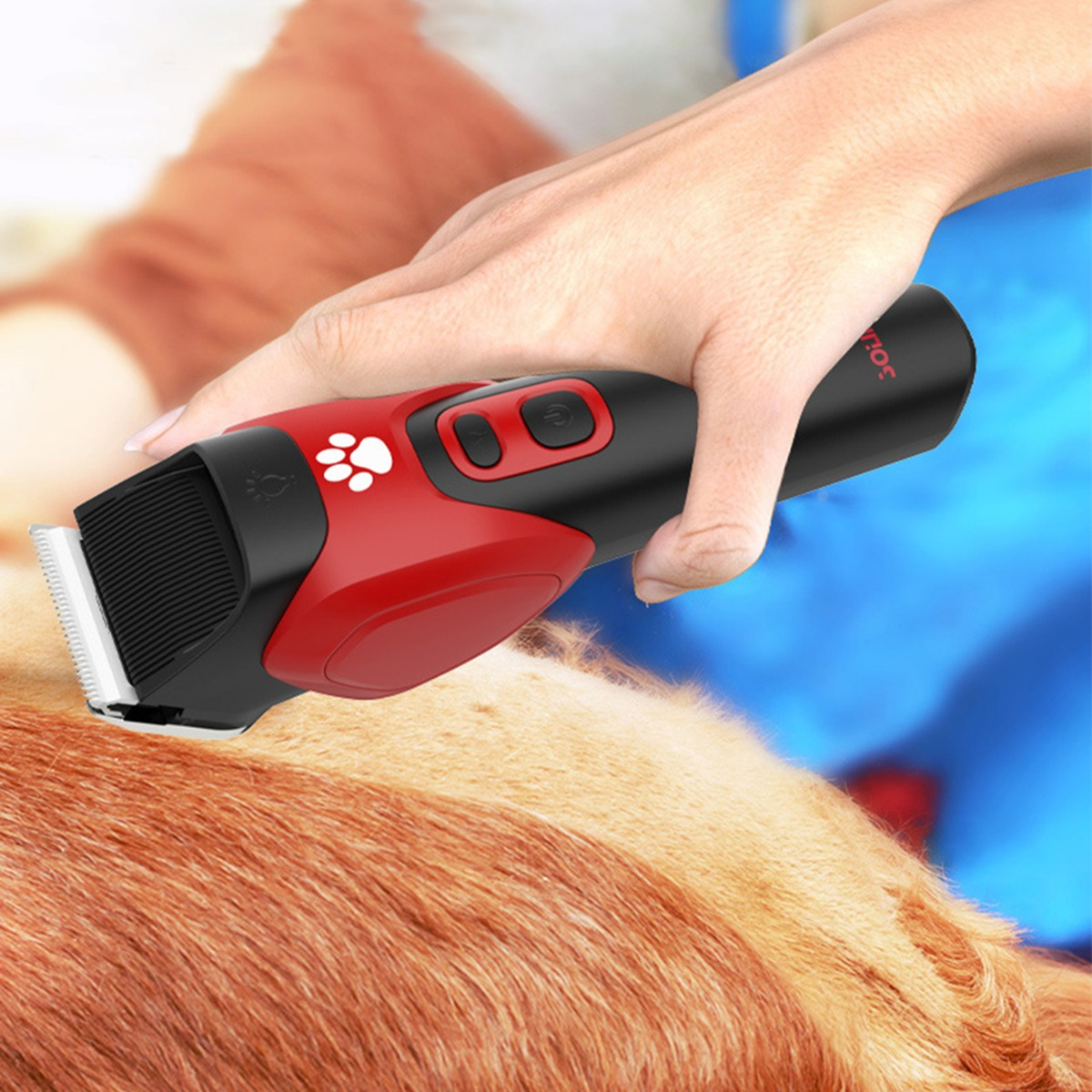 Eine Hand benutzt einen rot-schwarzen Haarschneider mit Pfotenabdruck, um das Fell eines Hundes zu pflegen.