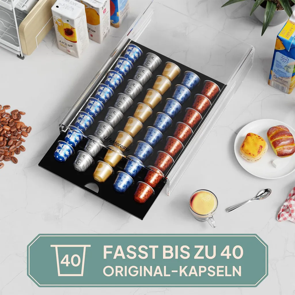 Transparente Kaffeekapselschublade mit bunten Kapseln auf einem Tisch, umgeben von Kaffeebohnen, Gebäck und einer Tasse Kaffee.